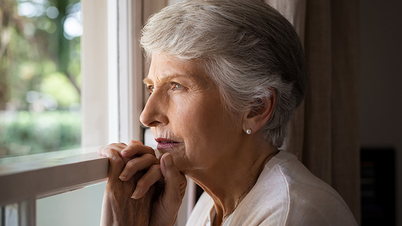 An elderly woman looks out a window.